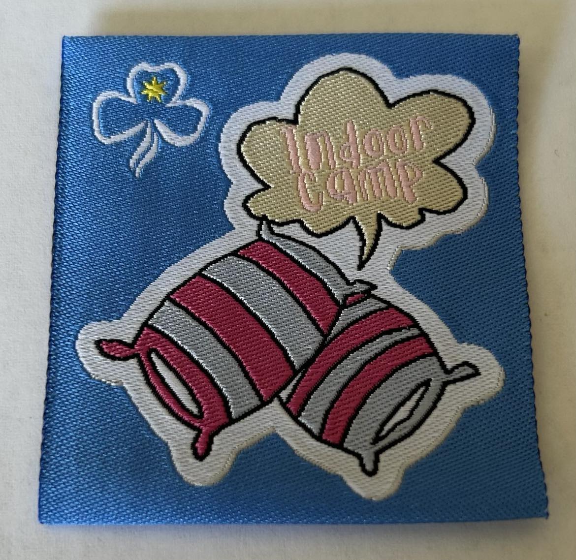 a square unbound blue badge with the words indoor camp and two pillows