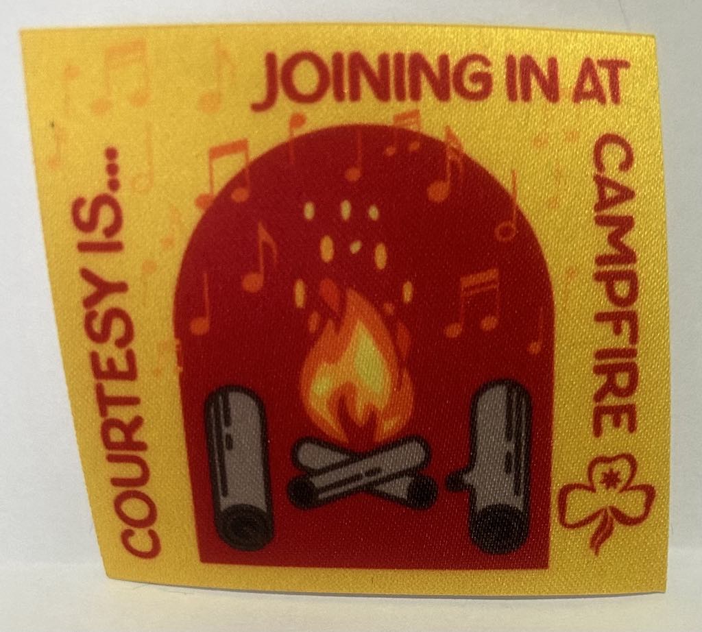 a square unbound badge with a yellow background with logs and a campfire and the words courtesy is joining in at campfire in red