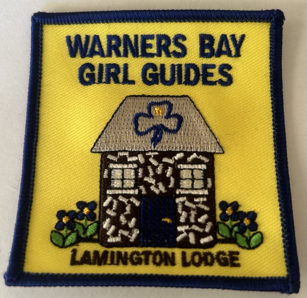 a square badge bound in blue that has a yellow background with a guide hut that is brown and white with the words warners bay girl guides lamington lodge
