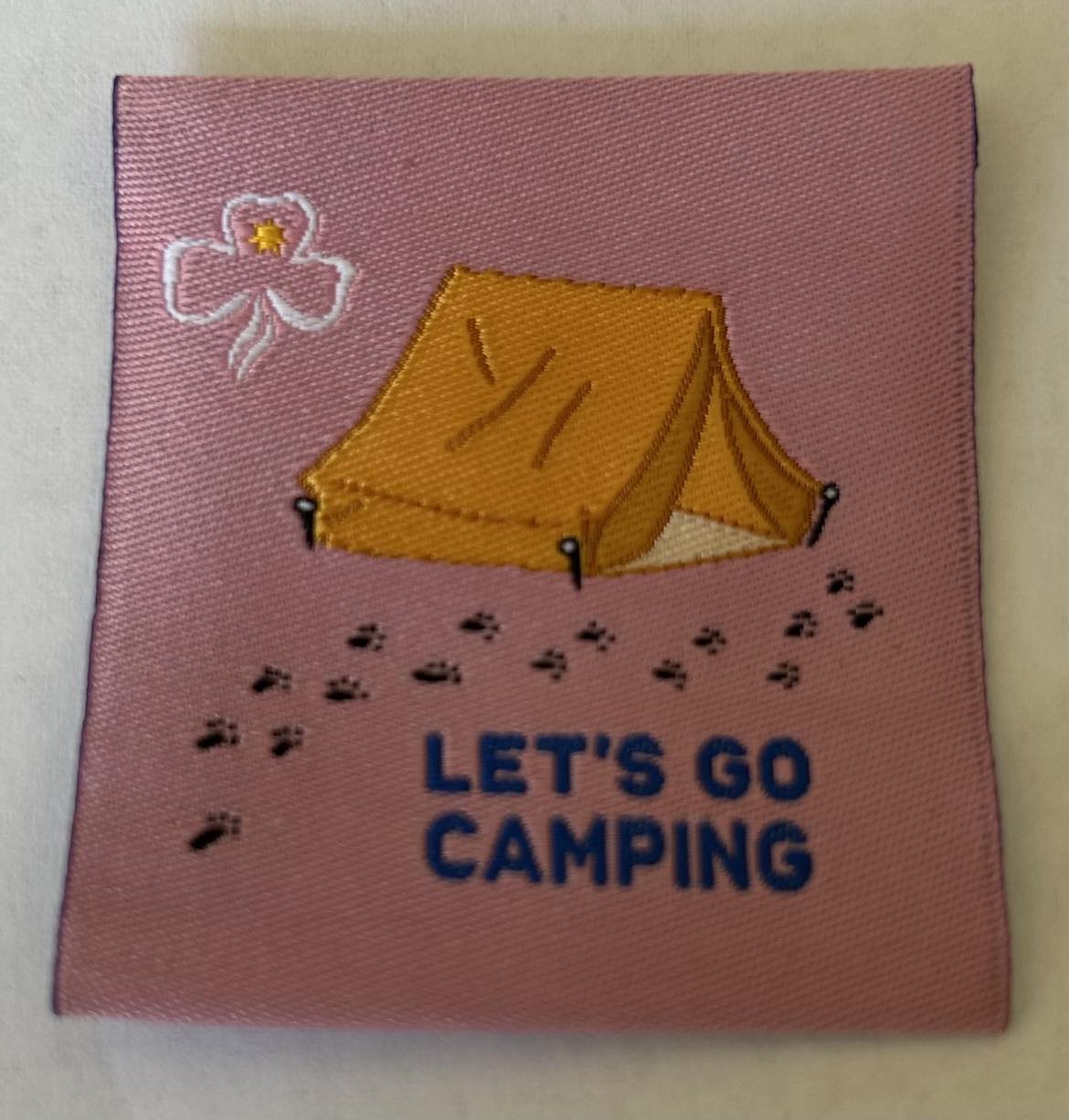 a square pink unbound badge with a tent and footprints and the words lets go camping