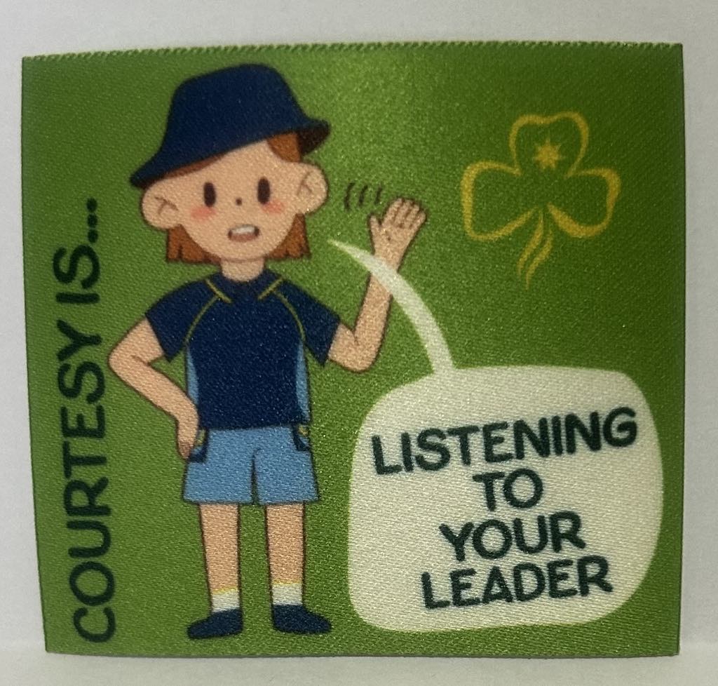 an unbound square badge that has a green background with a guide leader with a speech bubble and the words courtesy is listening to your leader