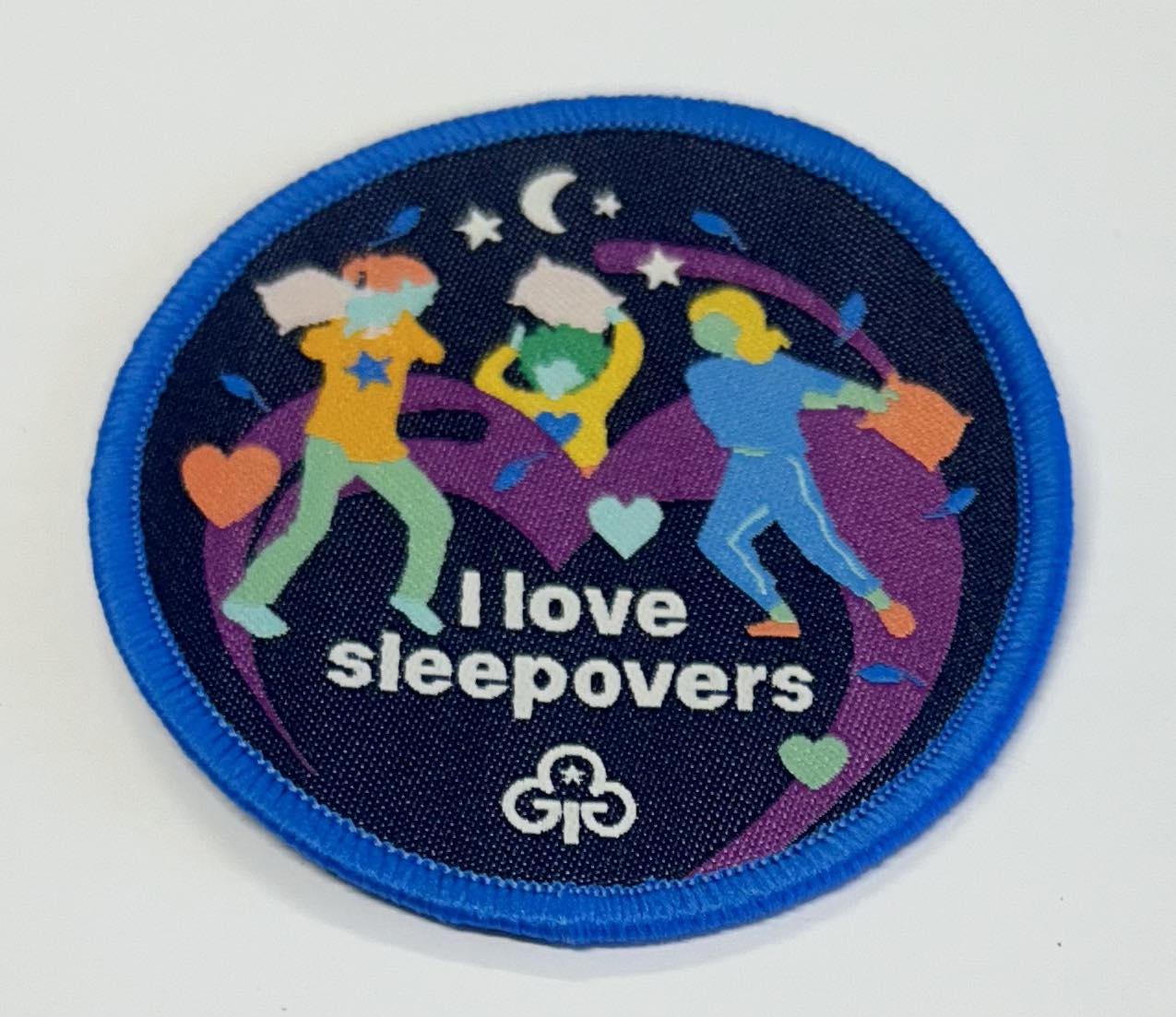 a round badge bound in blue with three girls having a pillow fight with the words I love sleepovers