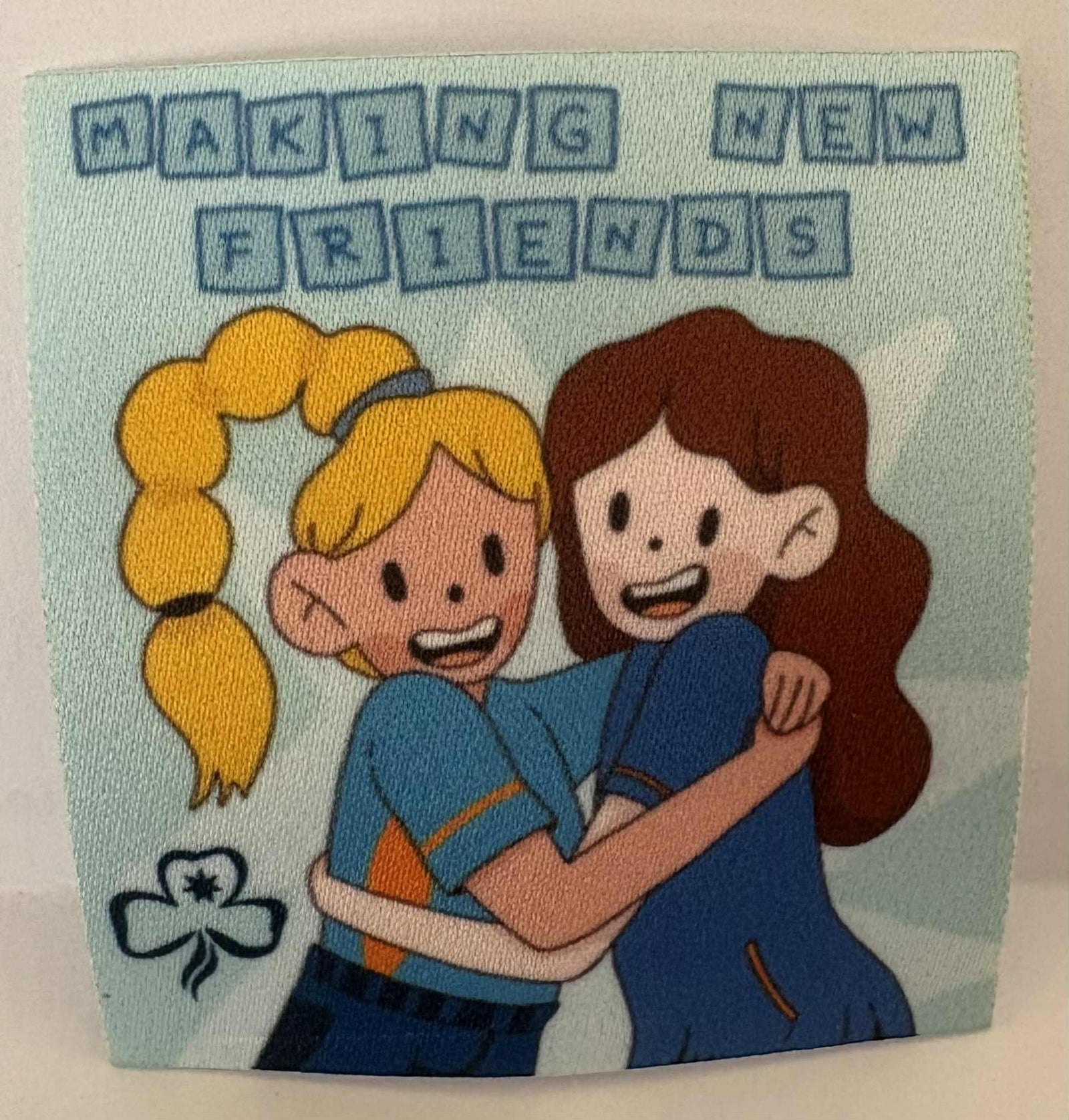 a square unbound badge with two girls hugging