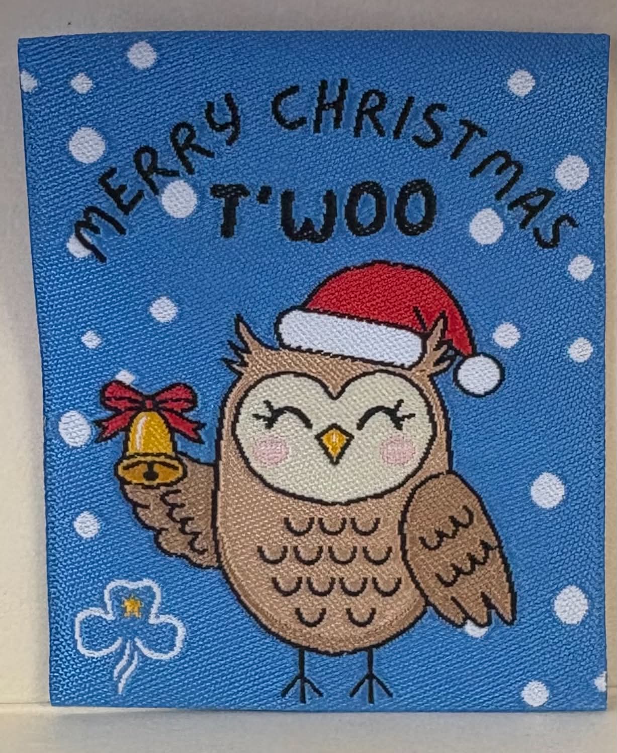 a square blue unbound badge with an owl with a gold bell and a Santa hat on