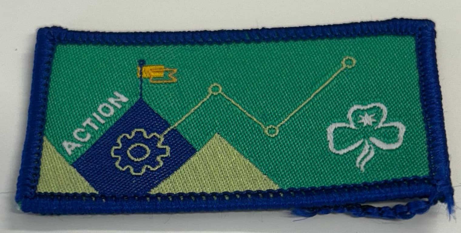 a bound rectangular badge with a cog, flag and a trefoil