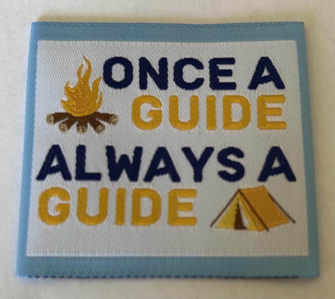 a square unbound badge bordered in light blue wth a campfire and a tent and the words once a guide always a guide