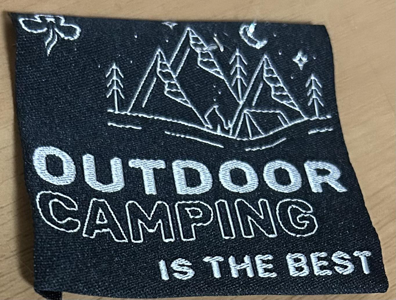 a black unbound badge with silver writing that says outdoor camping is the best and some silver trees and mountains