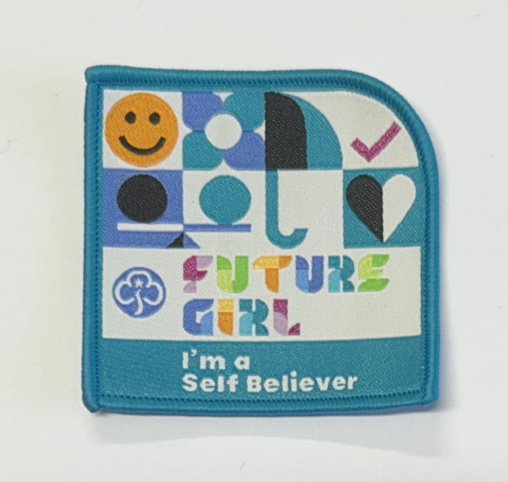 a square badge bound in bright blue with the words future girl I'm a self believer with a heart, umbrella and smiley face on it