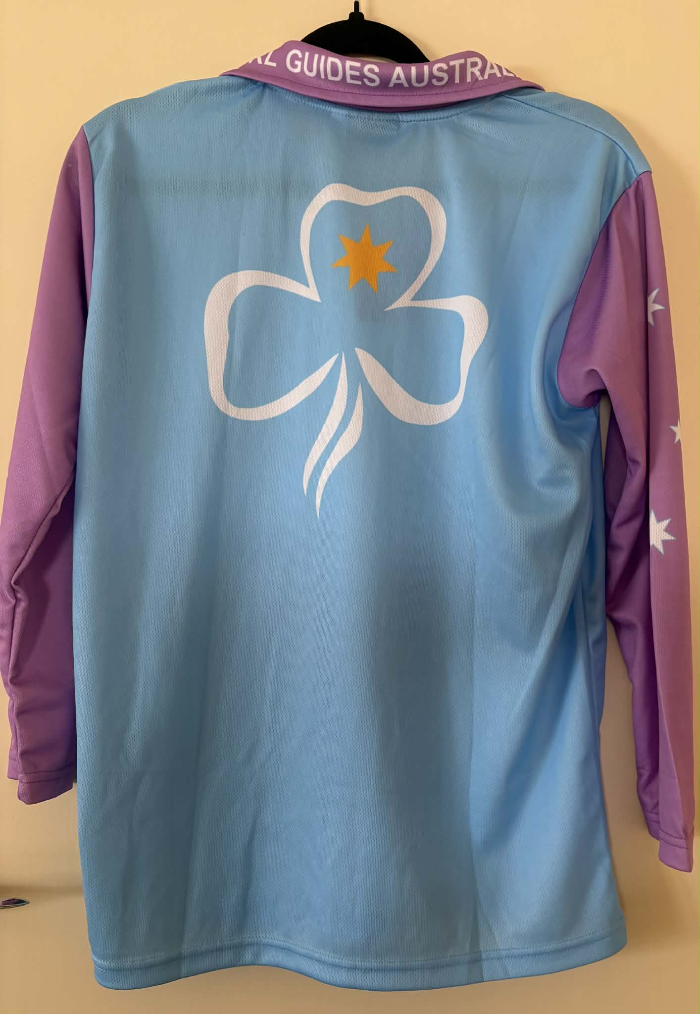Light blue and purple shirt with a trefoil and GGA on the front. Girl Guides Australia around the collar and a large trefoil on the back