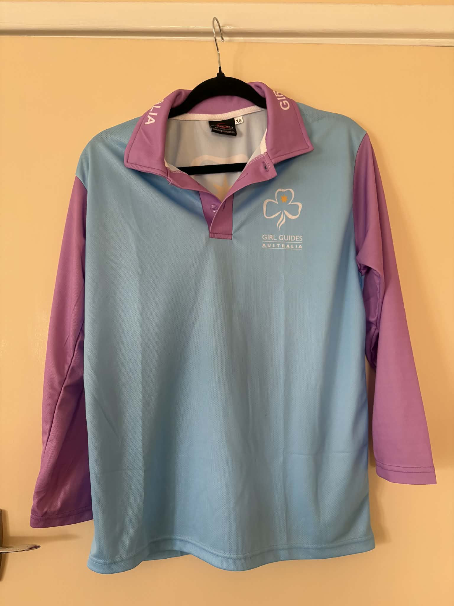 Light blue and purple shirt with a trefoil and GGA on the front. Girl Guides Australia around the collar and a large trefoil on the back