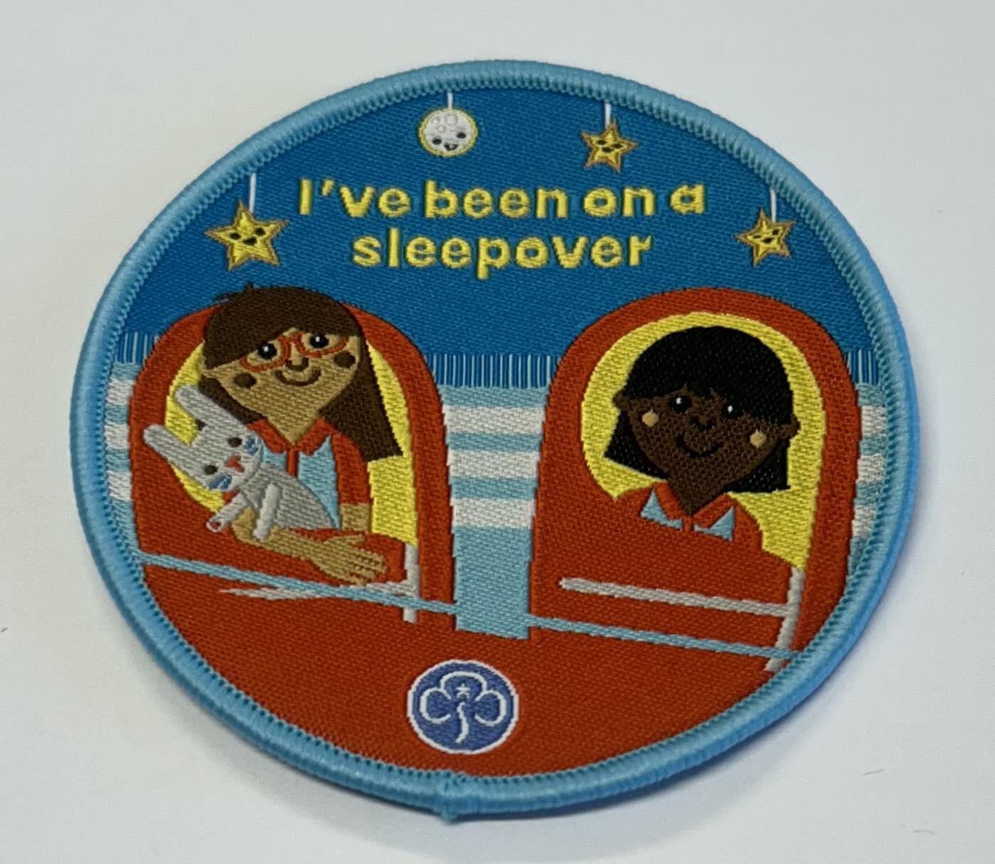 a round badge bound in blue with two girls in sleeping bags with stars overhead with the words I've been on a sleepover