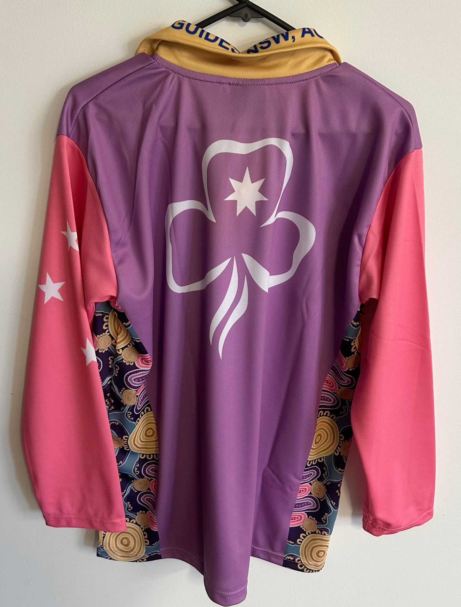a long sleeved polo shirt with pink sleeves, purple body with aboriginal art on the sides and a gold collar