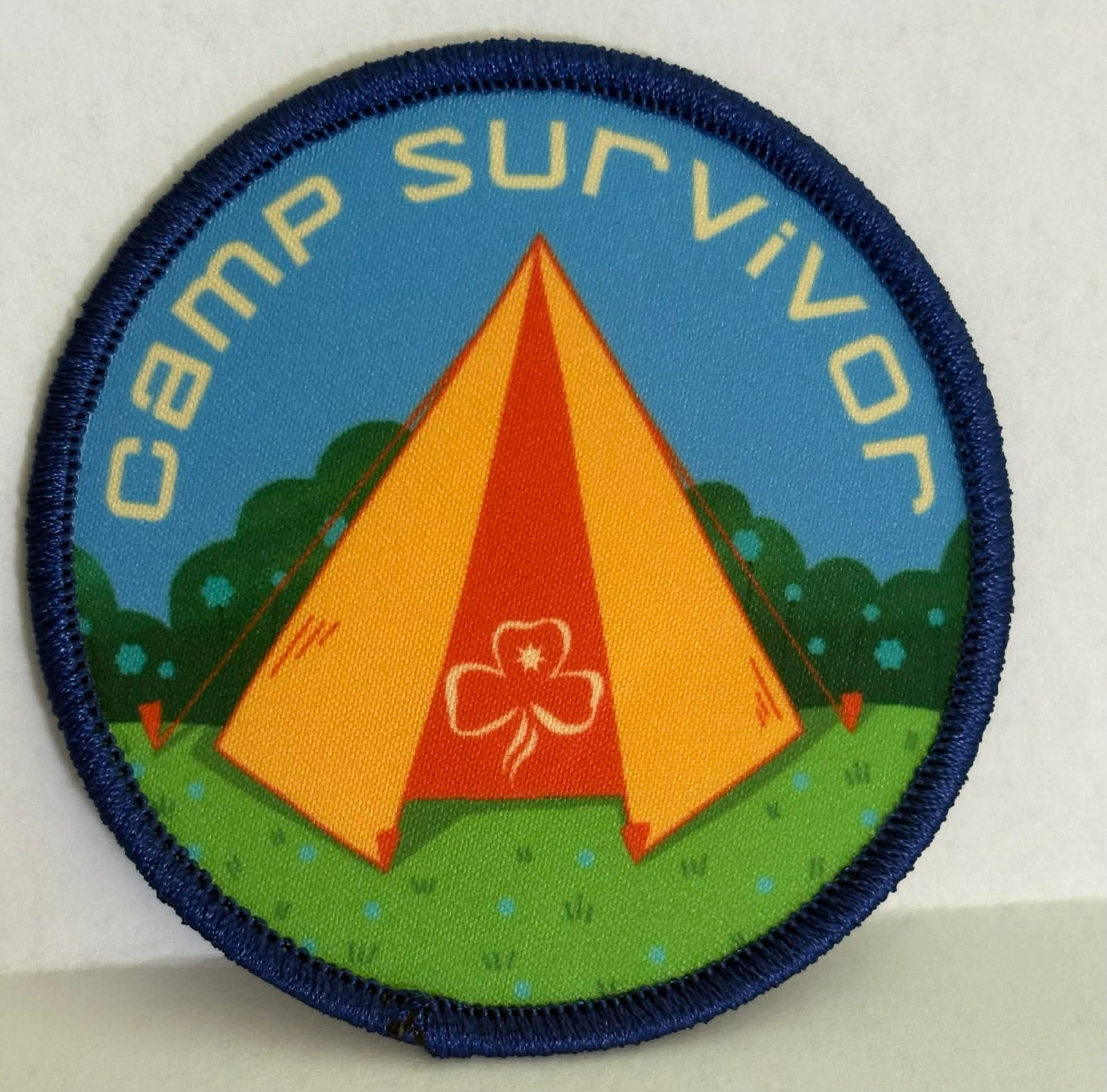 round and bound badge with a tent design and 'Camp Survivor' text on a blue background