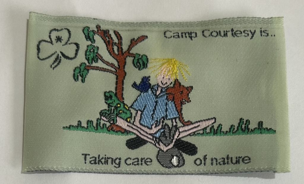 a rectangular unbound badge with a guide sitting under a tree with animals with the words camp courtesy is taking care of nature