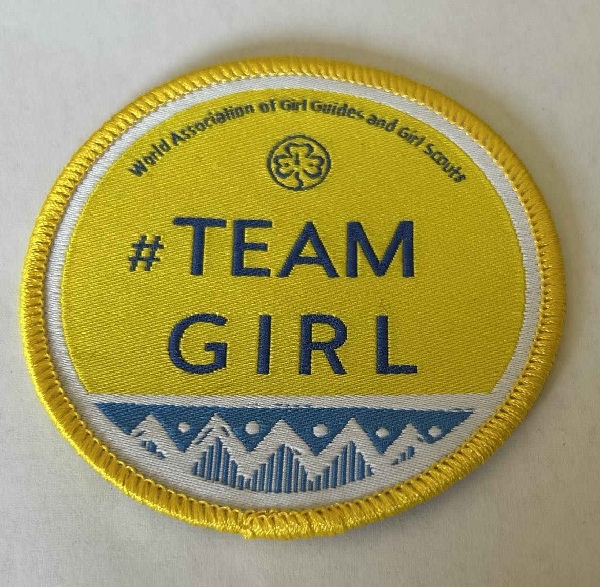 a round yellow badge bound in yellow with team girl written in blue