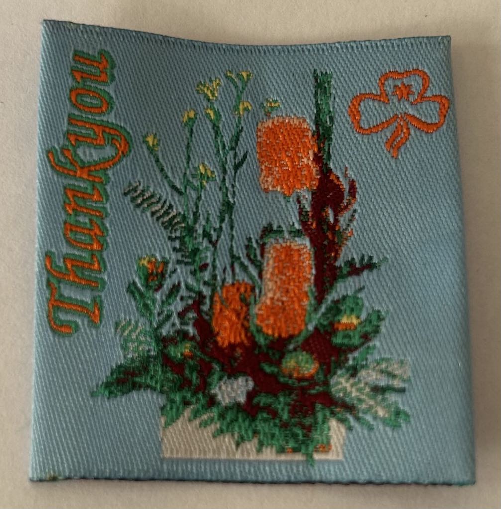 a light blue square unbound badge with the words thank you in orange and a bunch of native flowers