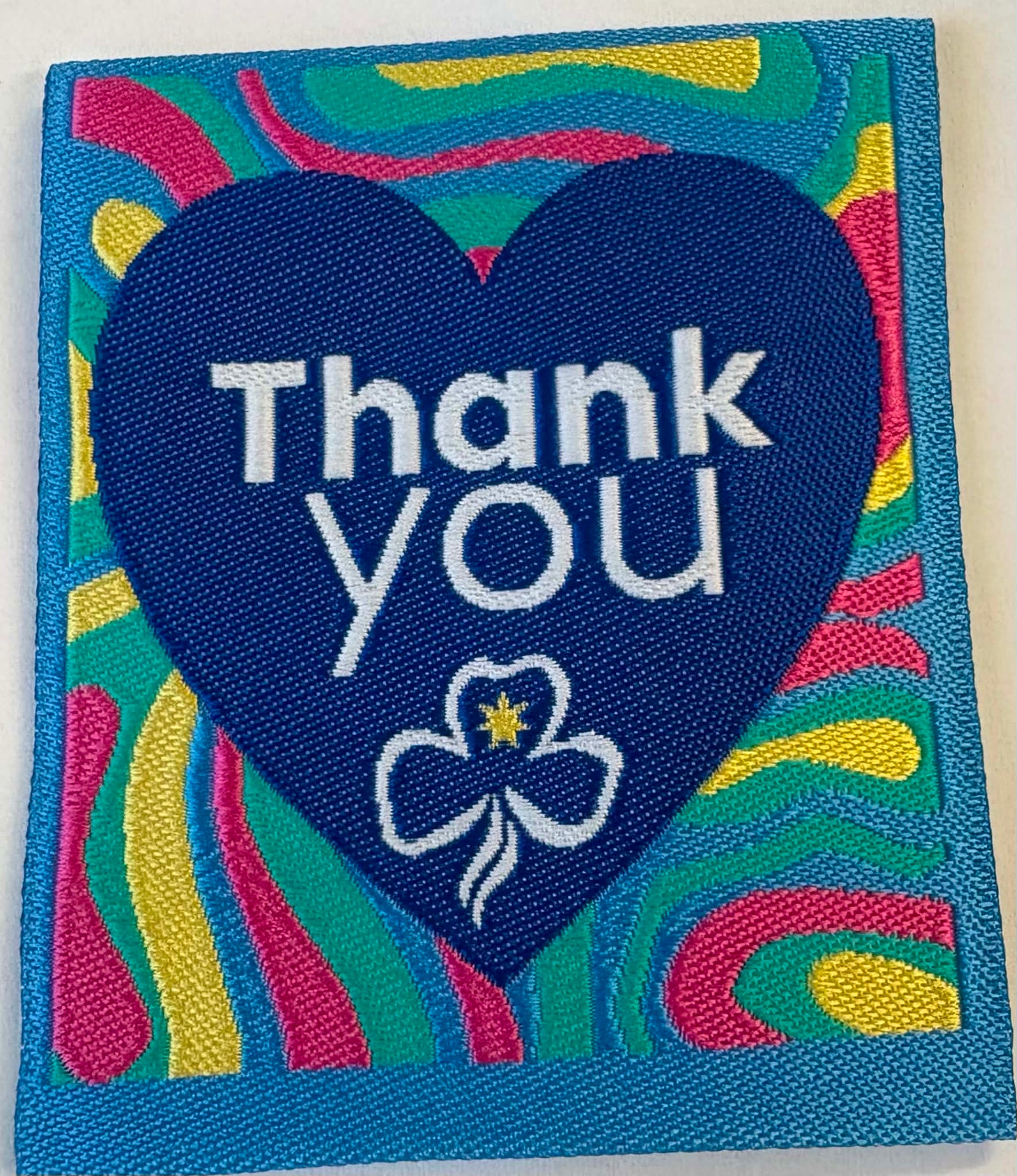 a square unbound badge with the words thank you and a trefoil inside a blue heart with pink, yellow and green swirls in the background