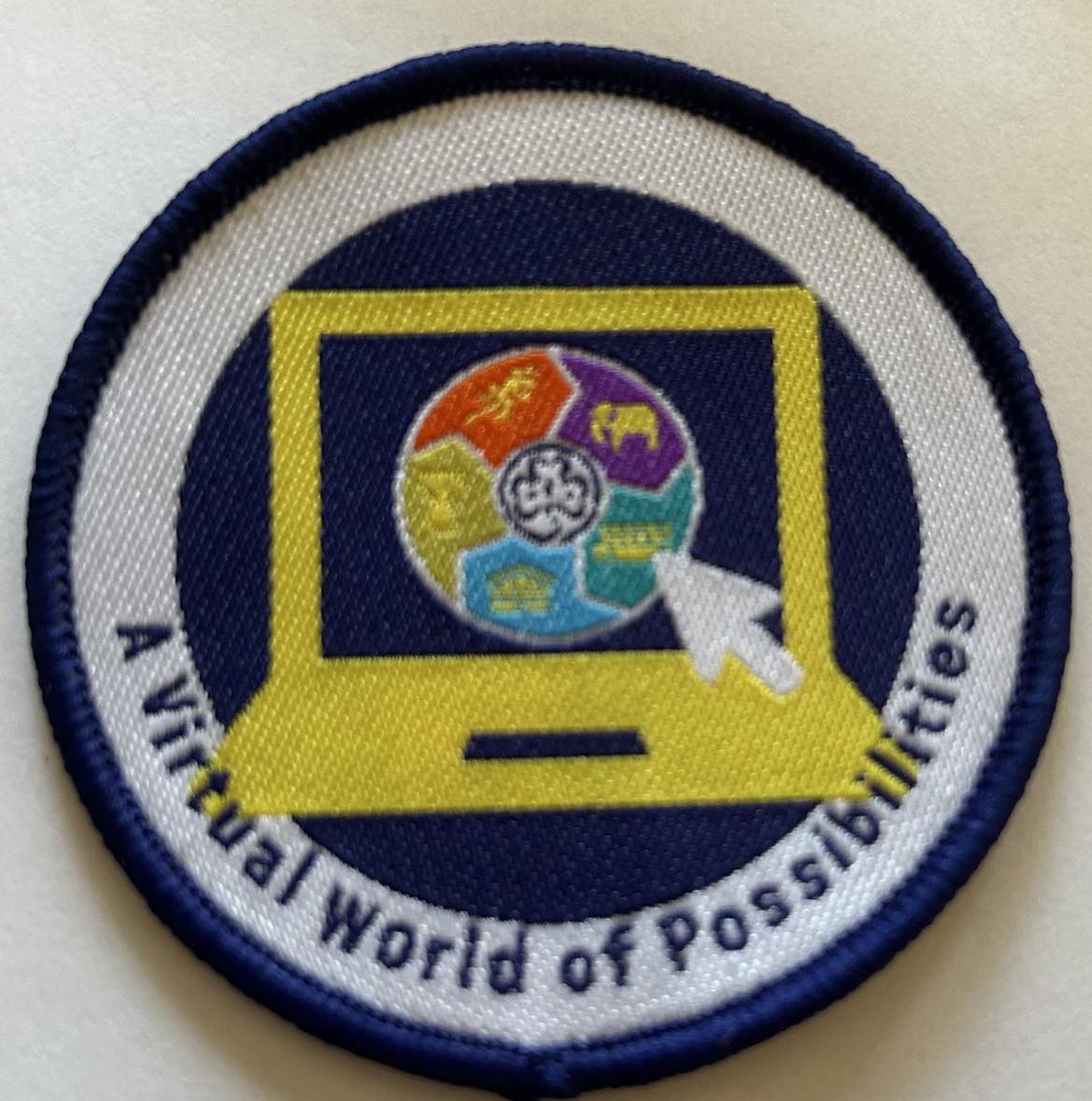 a round badge bound in blue with a laptop with a round badge with the world centres n it with a trefoil in the middle