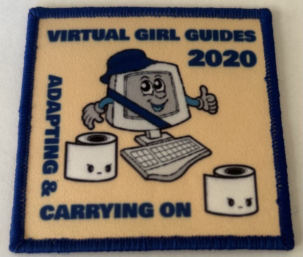 a square cream badge bound in blue with a computer and two toilet paper rolls and the words adapting and carrying on