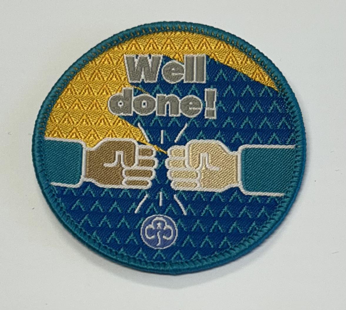 a round badge bound in green with a blue and gold background with two fists pumping with the words well done