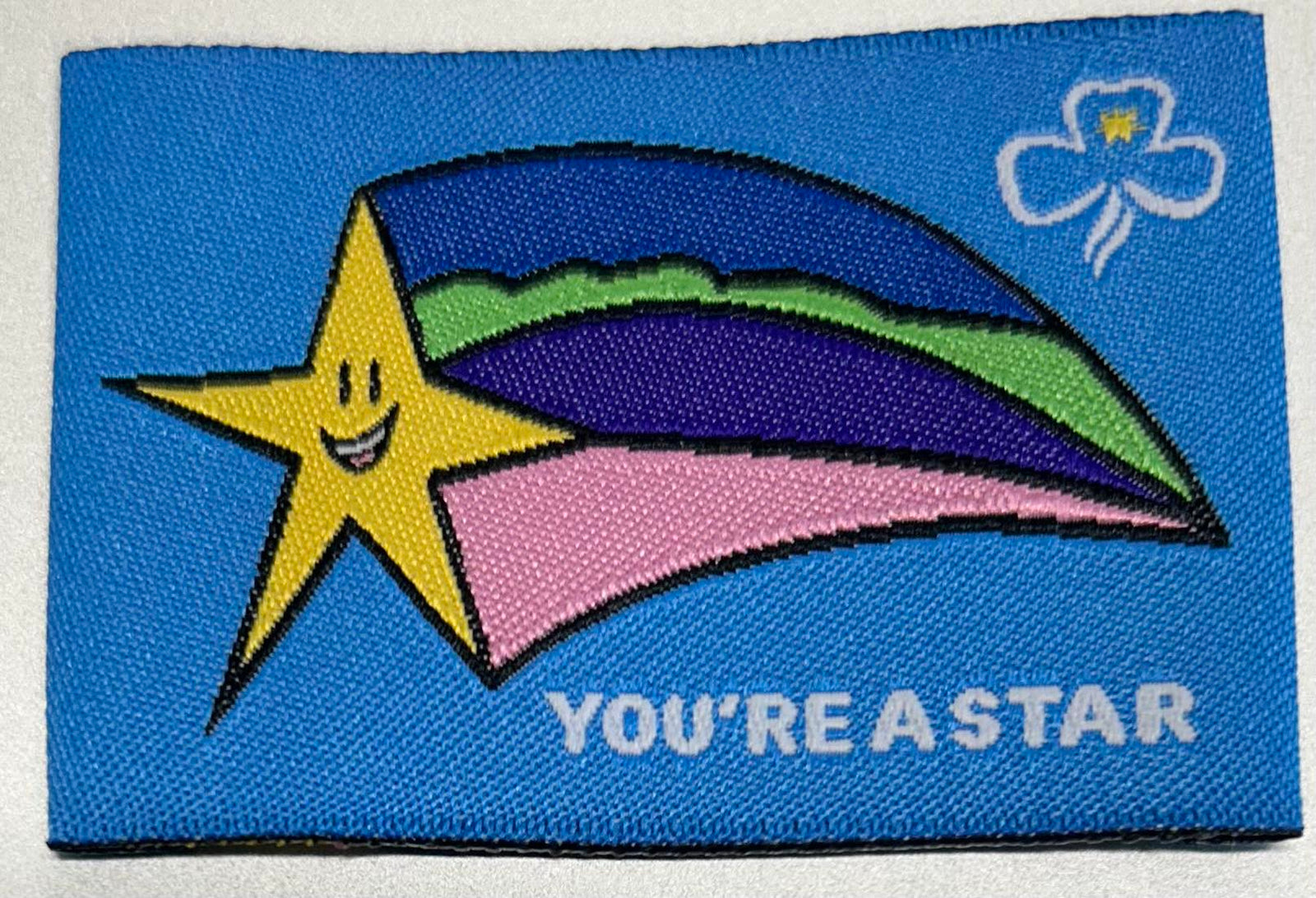 an unbound rectangular badge that is light blue background with a yellow star with coloured stream behind the star